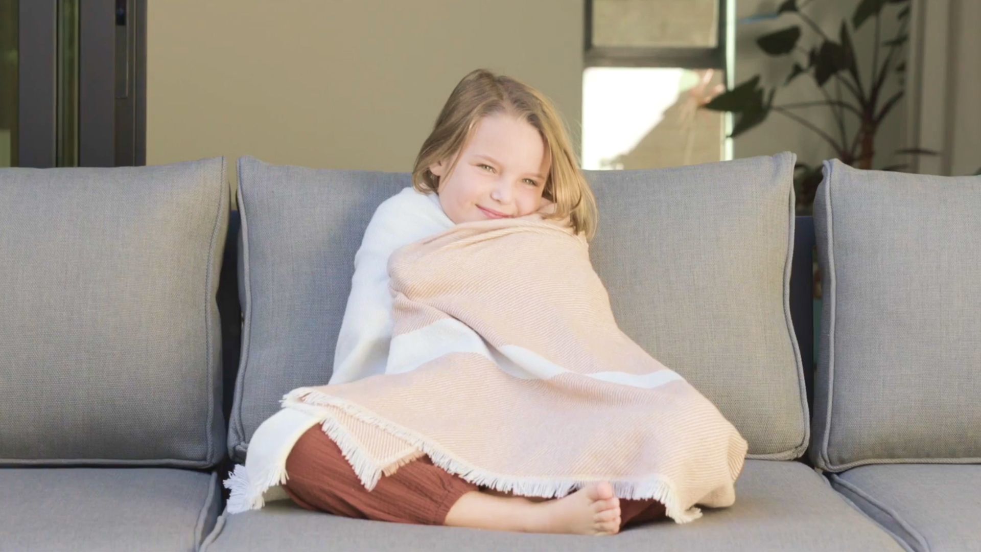 Person relaxing on an outdoor sofa with Outer’s bug-repellent throw blanket in Sierra Orange Colorblock https://liveouter.com/