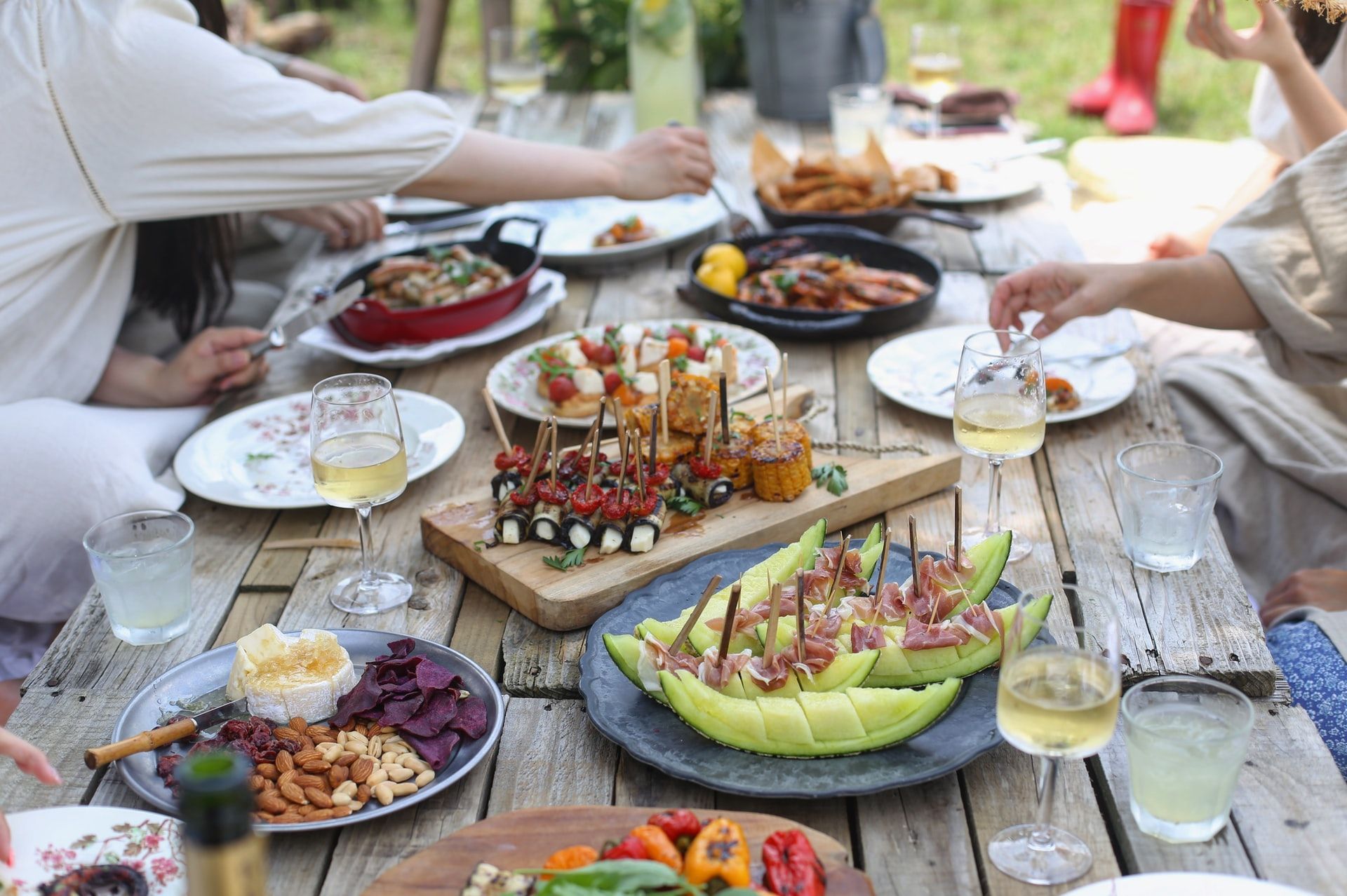 A wooden outdoor dining table laden with delicious food for a backyard party.