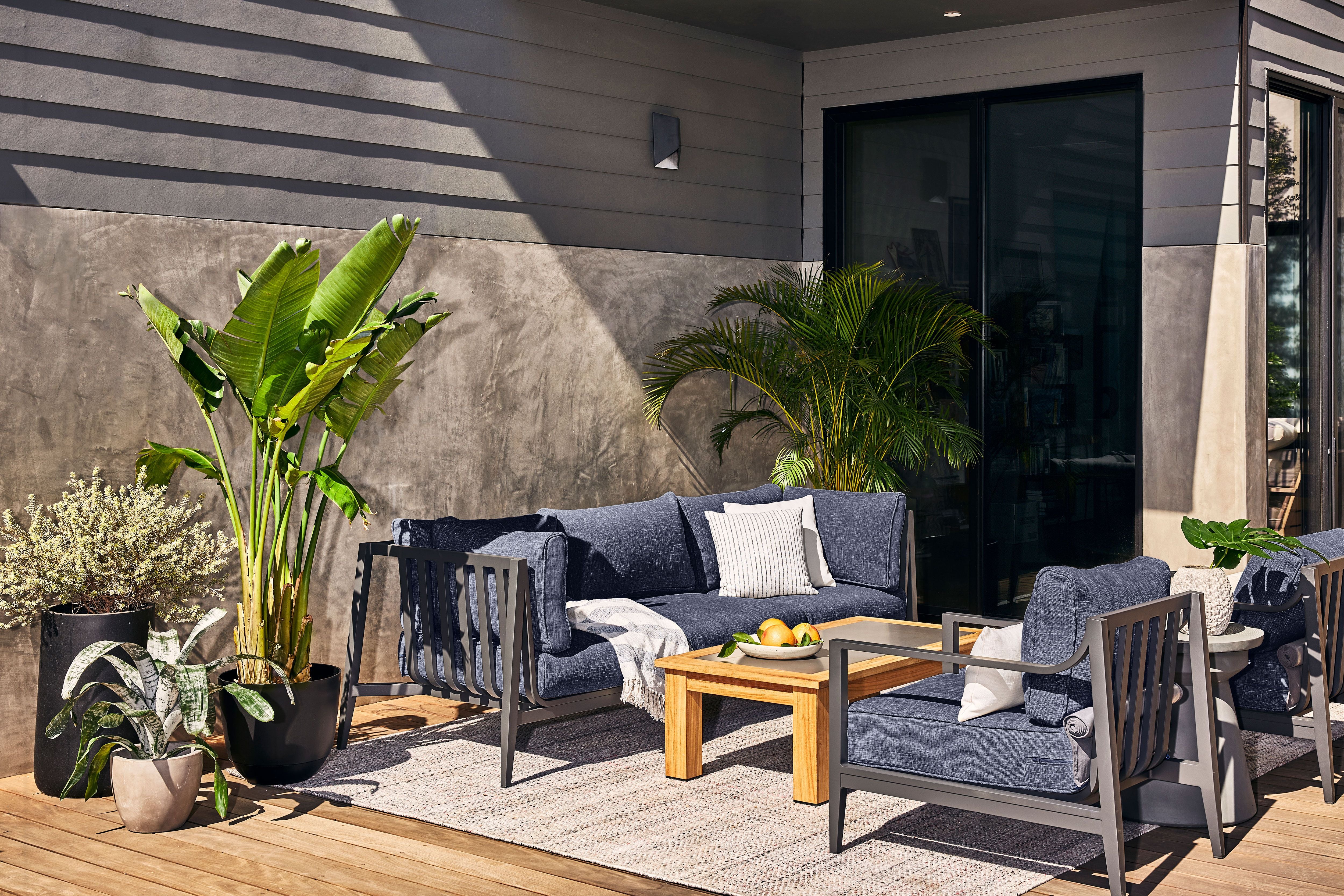 The 3 seat charcoal aluminum sofa and two armchairs shown on a sunny day with navy fabric and the sand dune beige outdoor rug.
