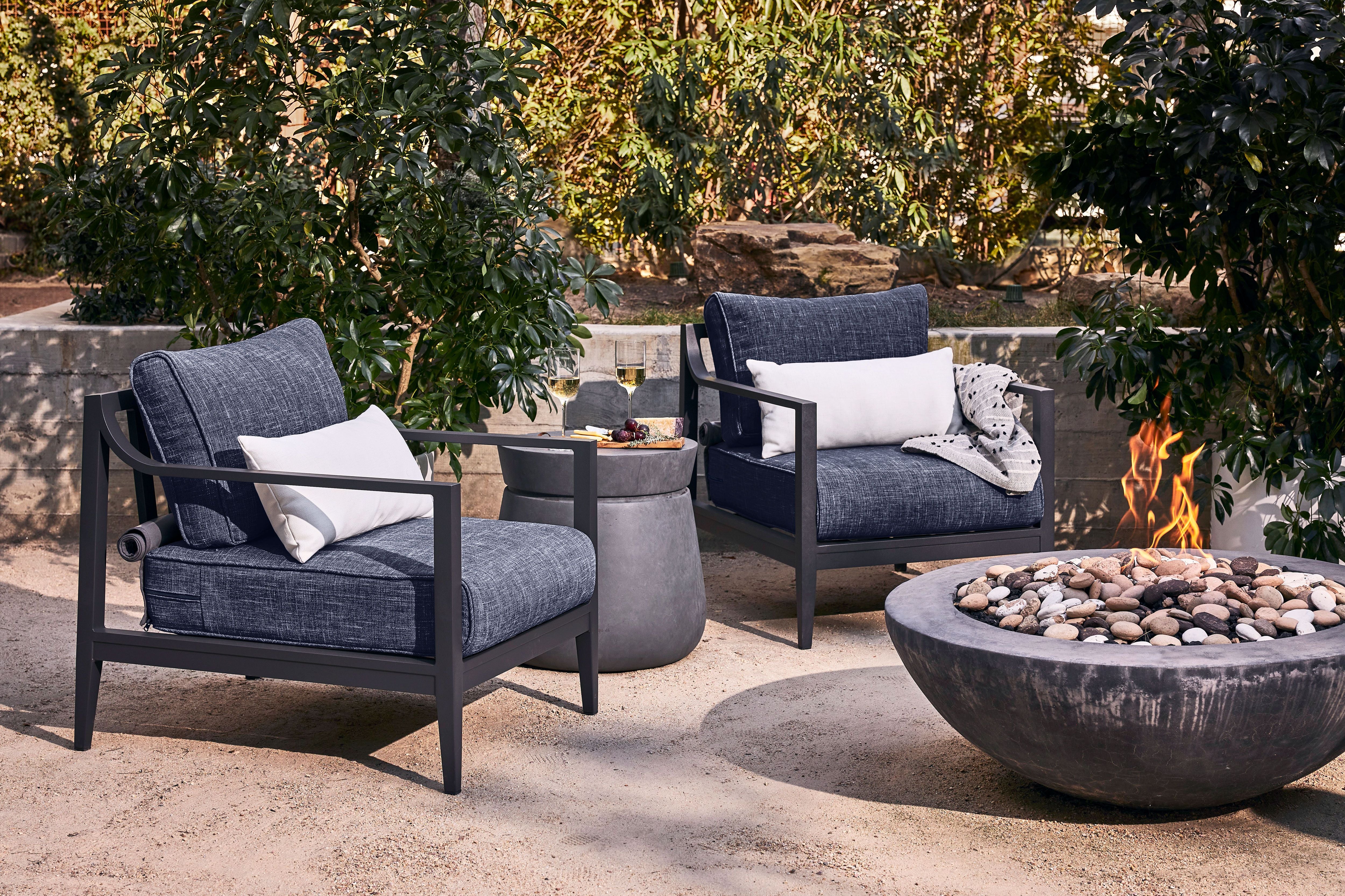Two outdoor charcoal aluminum armchairs with navy fabric on a decomposed granite surface next to a fire pit.