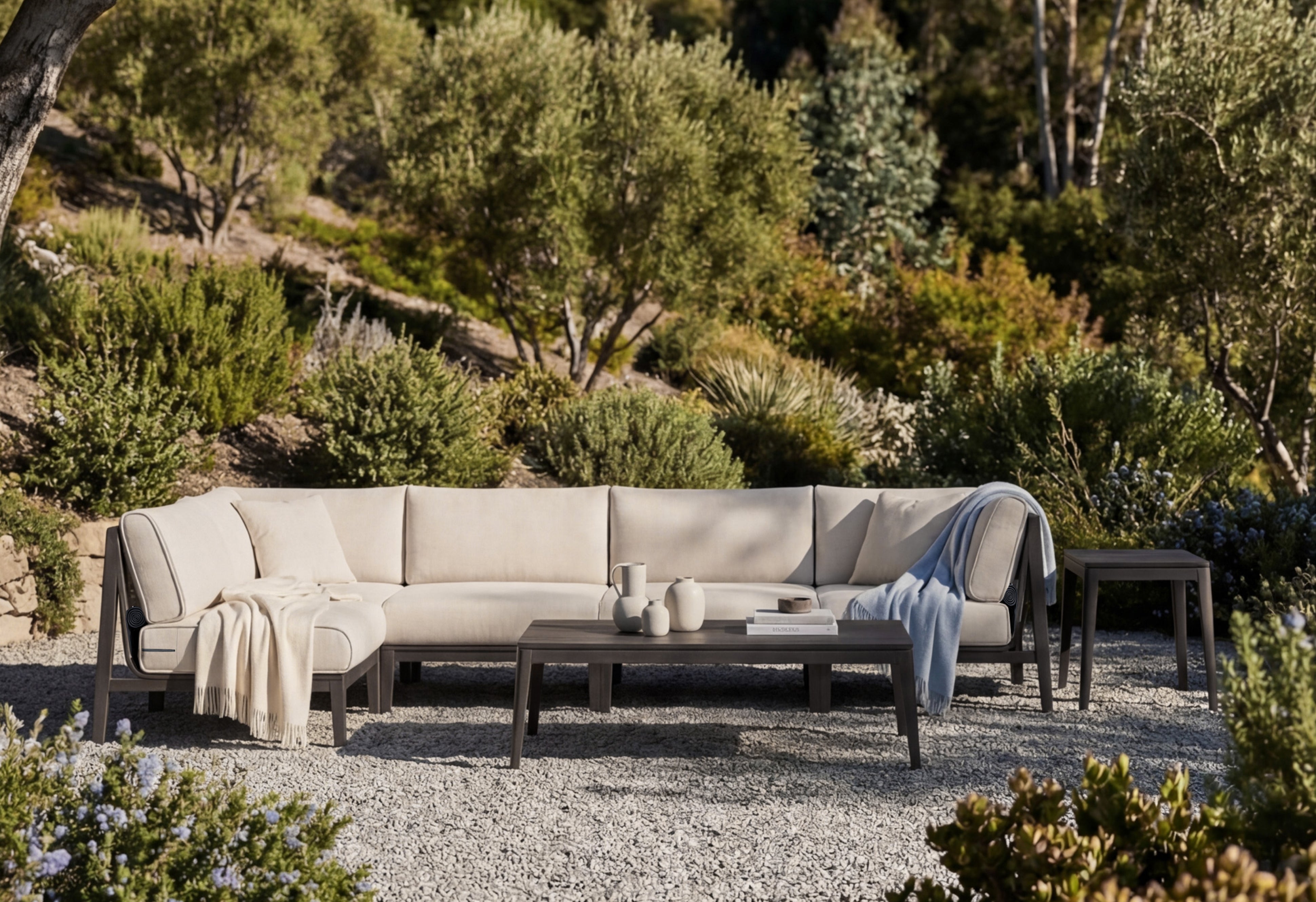 Modern outdoor sectional sofa with aluminum frame and coffee table in landscaped garden patio setting with gravel and greenery