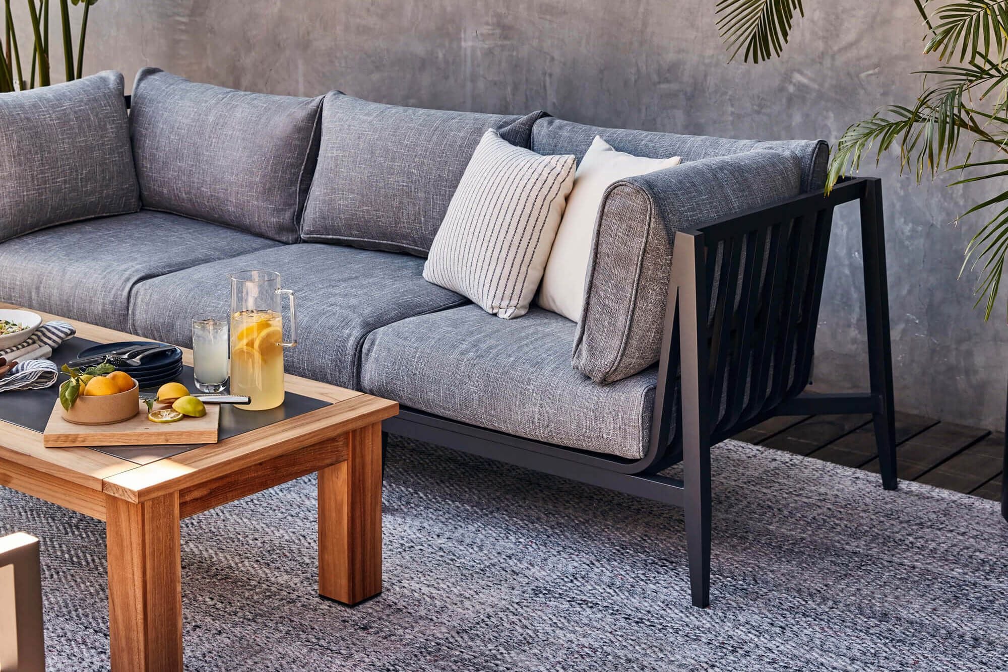 A closeup of the charcoal aluminum outdoor sofa showing the detail of the pacific fog gray fabric and the pebble gray outdoor rug it's sitting on. #color_pacific fog gray