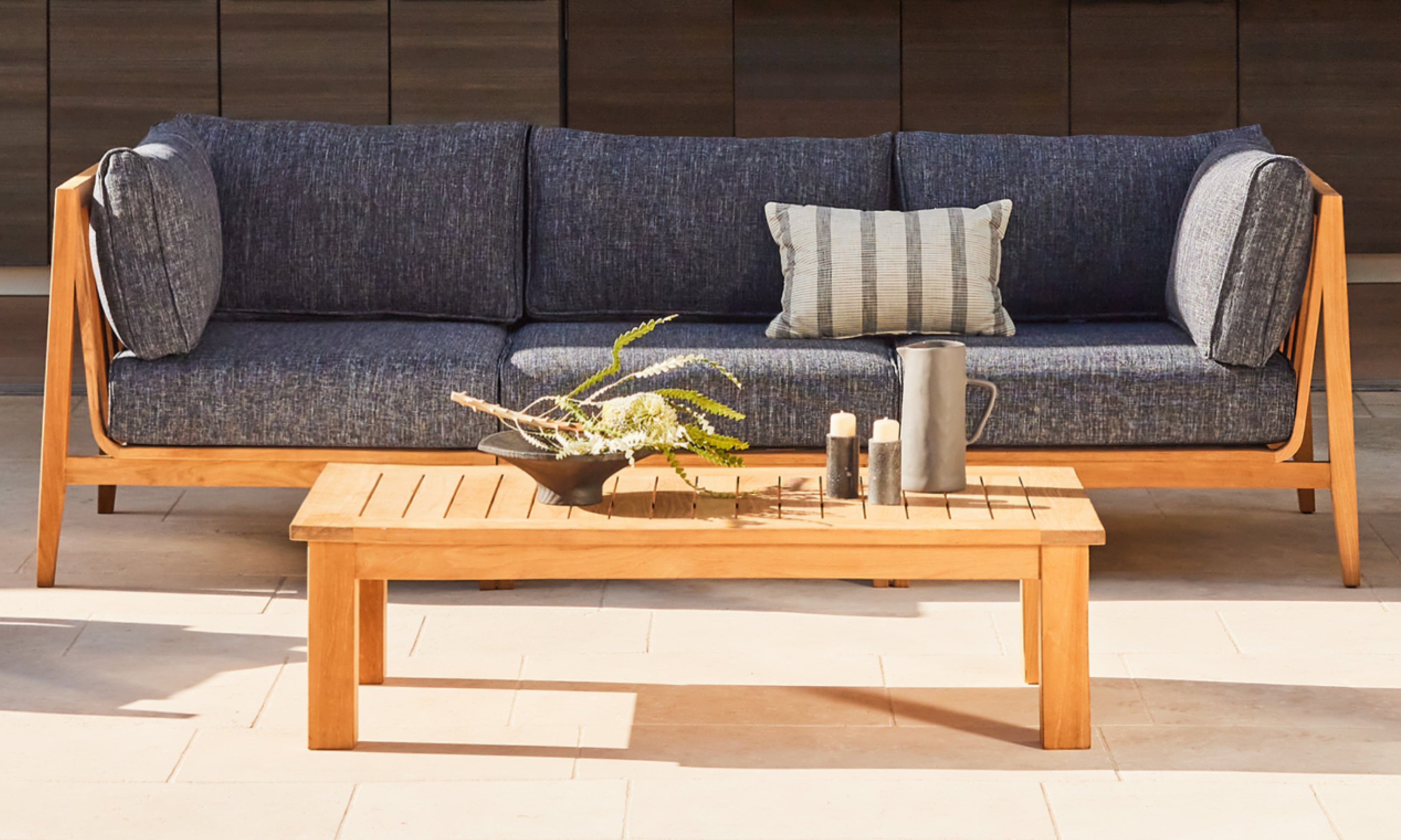 Outer teak outdoor coffee table paired with modern sofa featuring charcoal cushions on contemporary patio