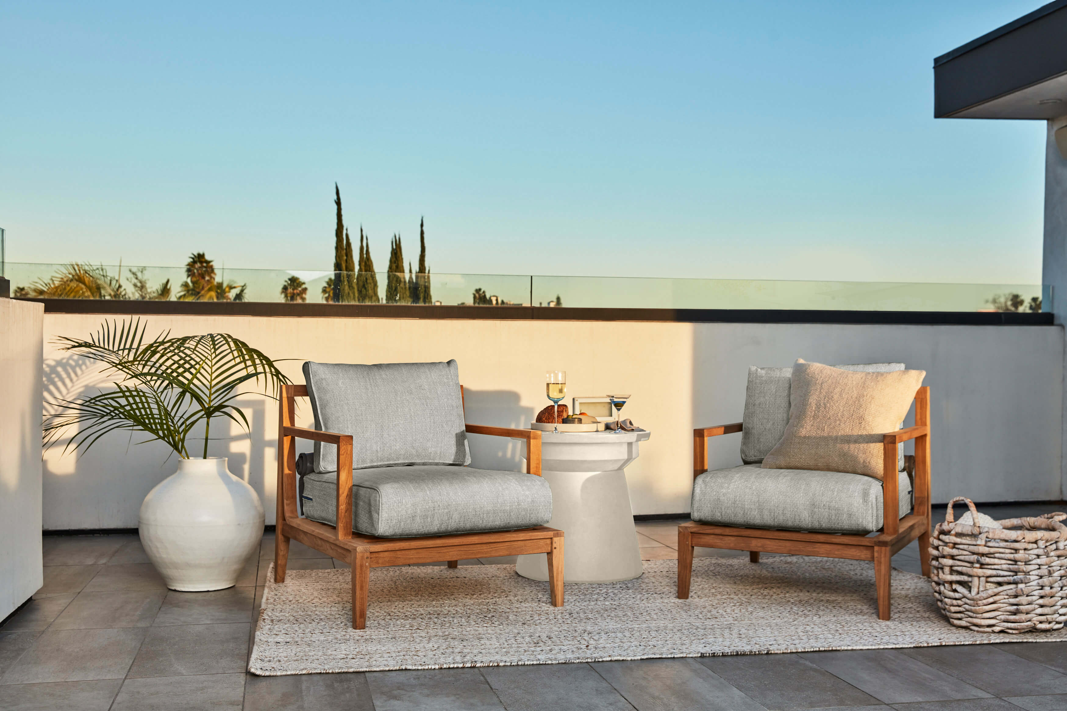 The white Concrete Side Table in Classic design shown on a patio with two teak armchairs. #table color_(unavailable) white