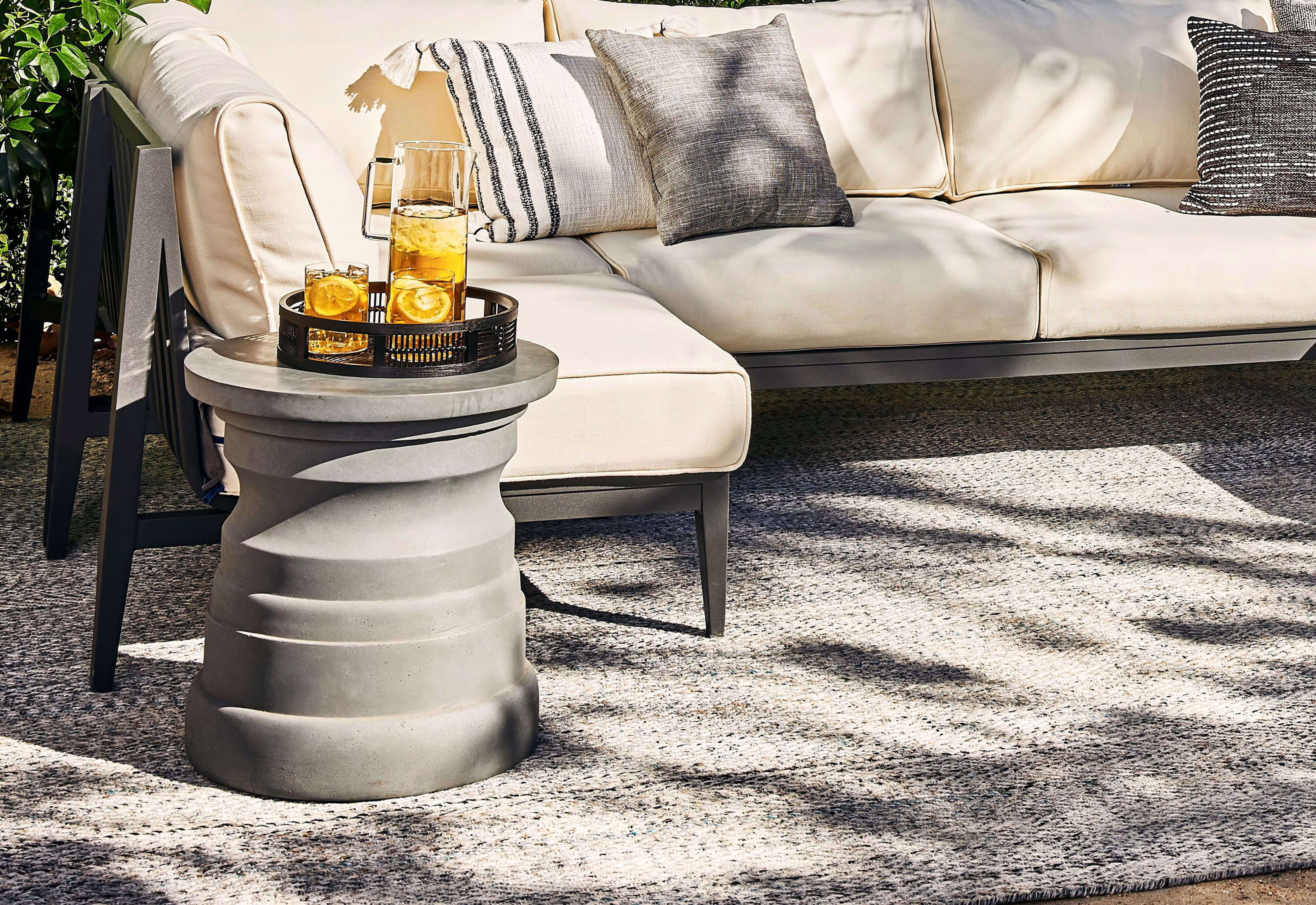 The gray Tiered Concrete Outdoor Side Table coordinated with an Outer aluminum L sectional in cream. #table color_gray