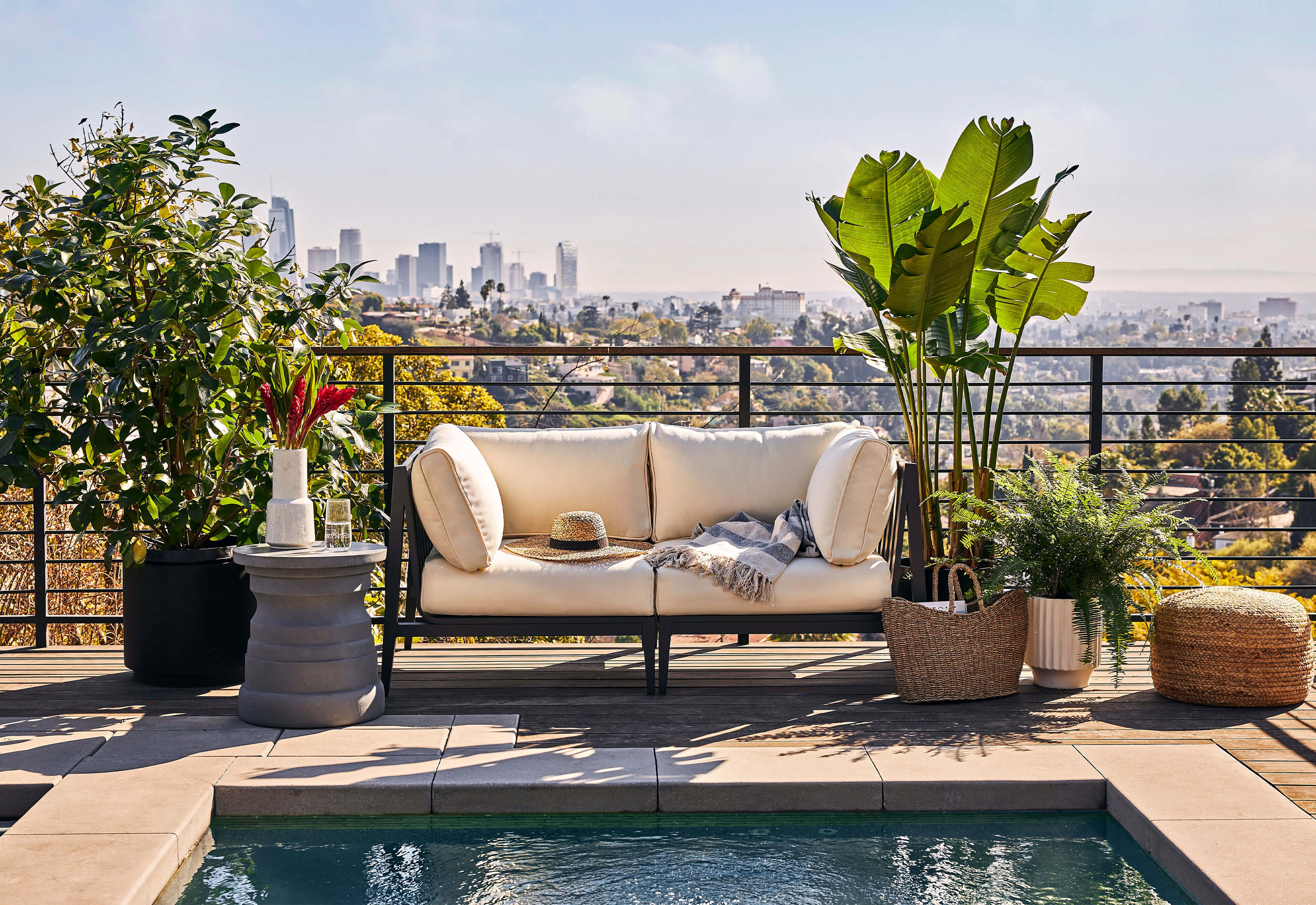 The gray Tiered Concrete Outdoor Side Table on a rooftop patio beautifully coordinated with the cream and aluminum loveseat.