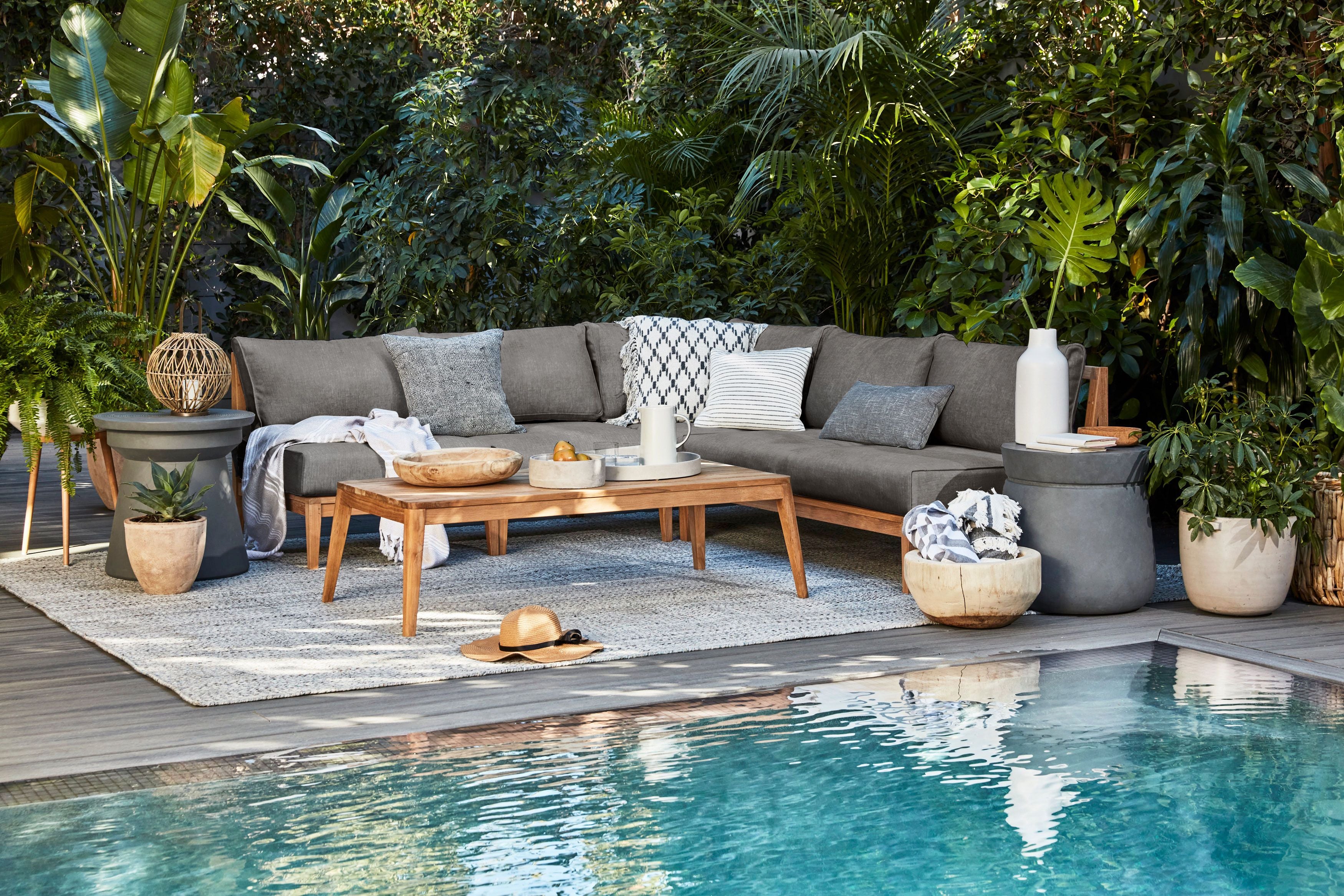 The FSC certified teak U sectional in pebble gray shown poolside with the sustainable outdoor teak coffee table with tapered legs.