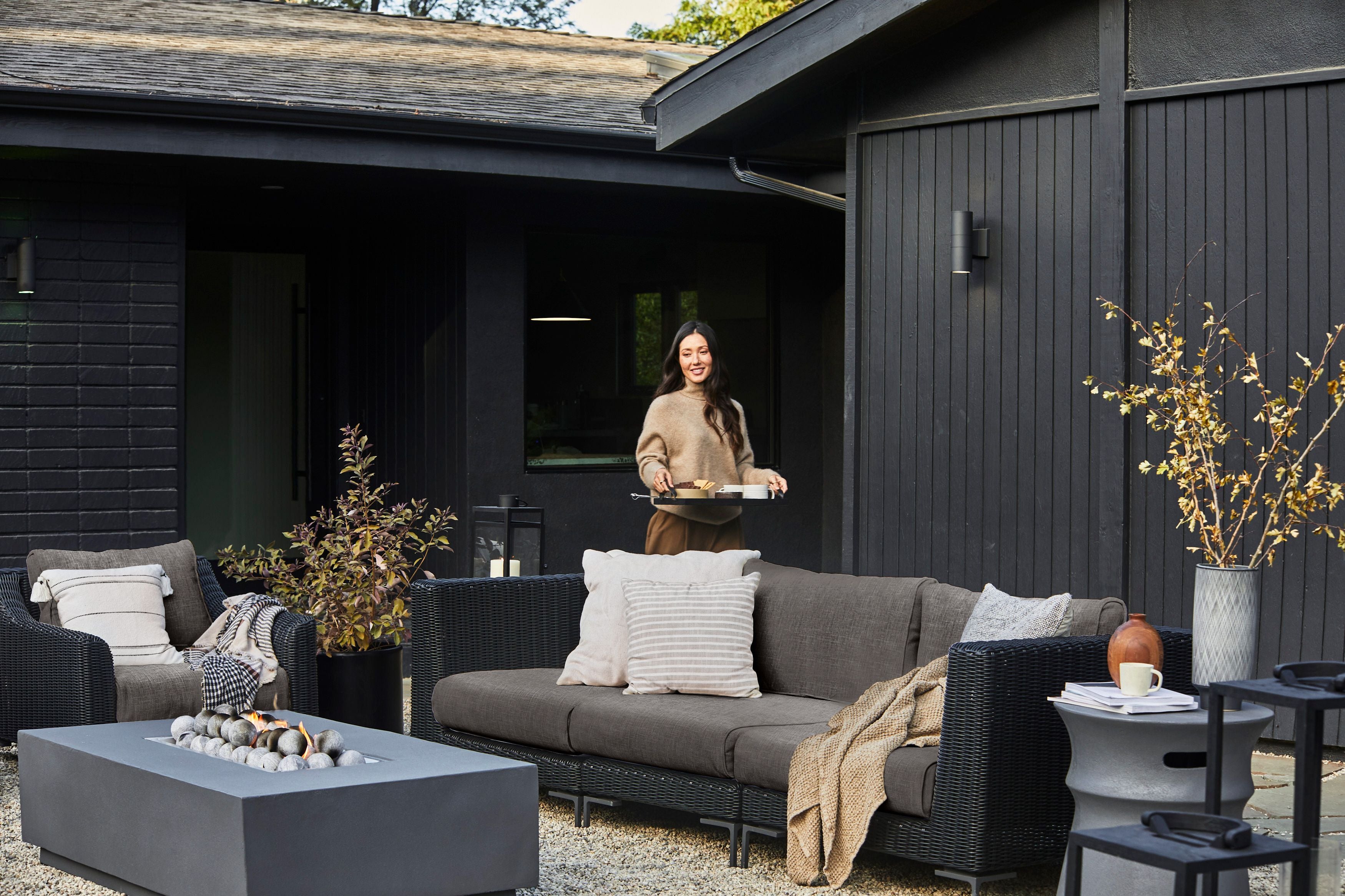 The black wicker outdoor sofa and armchair in dark pebble gray shown in a backyard on a gravel surface.