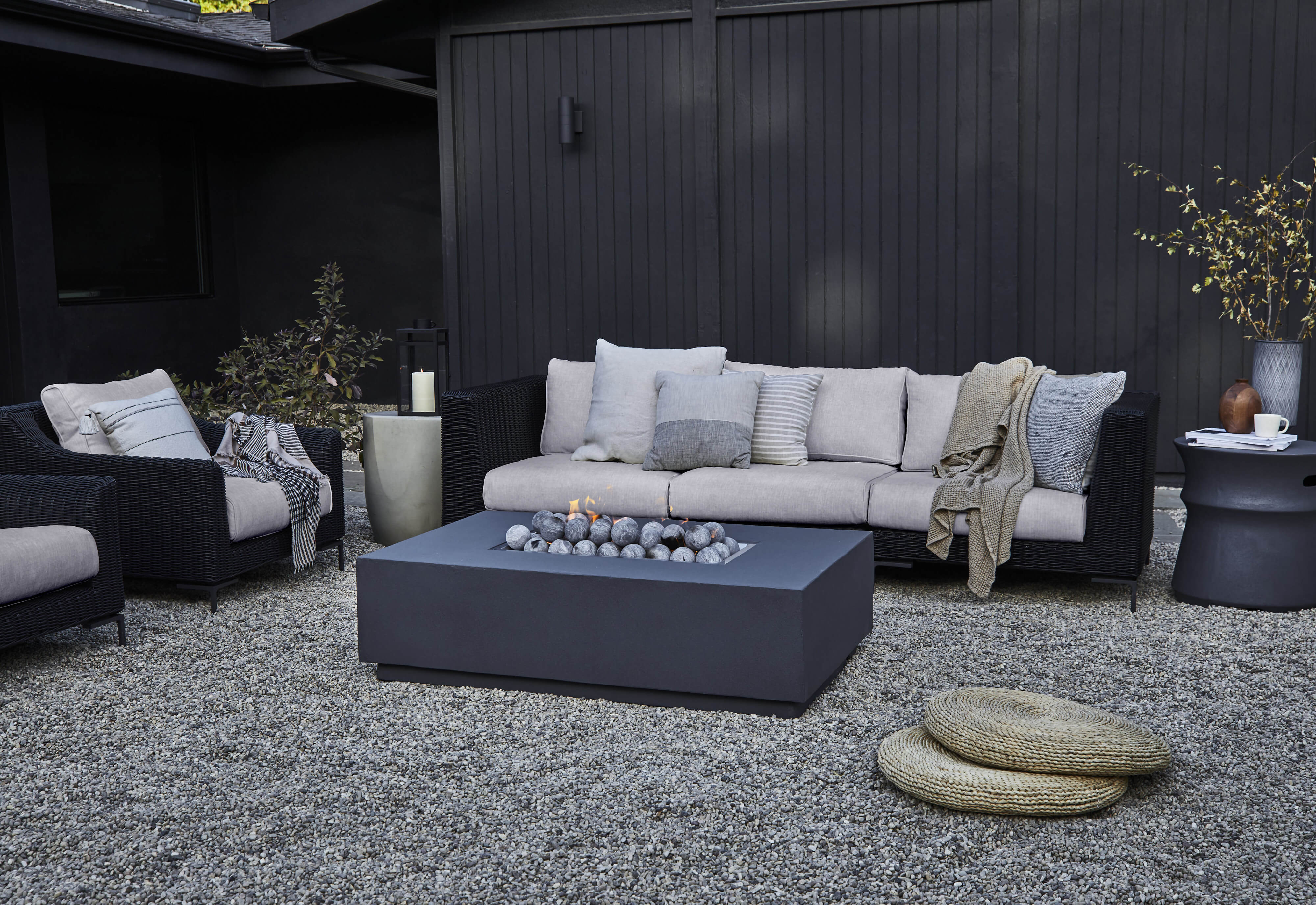 Black wicker with sandstone gray cushions in a 3 seat sofa and armchairs featured on a gravel substrate.