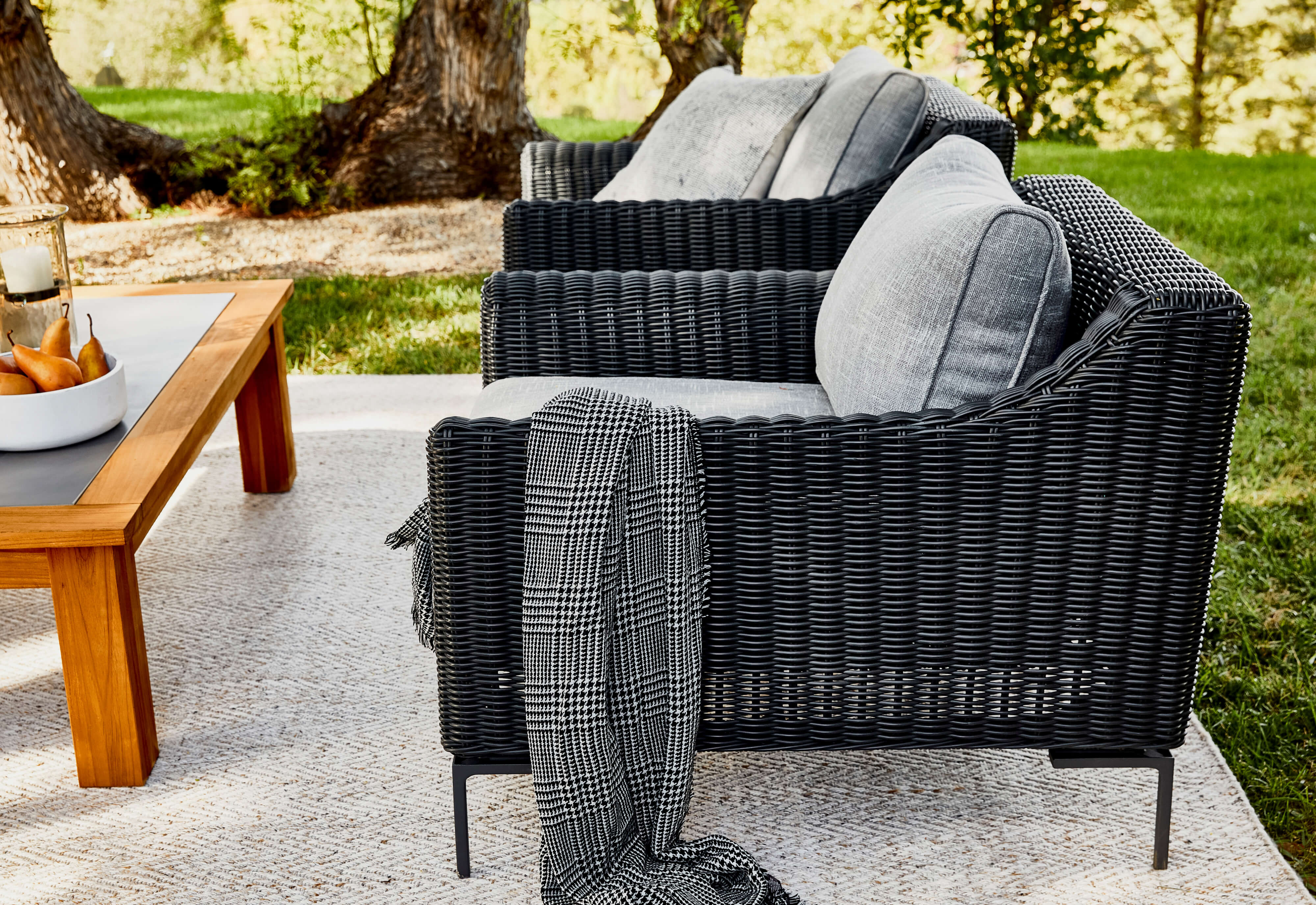 Black wicker armchairs with pacific fog gray cushions and draped houndstooth outdoor bug shield blanket.