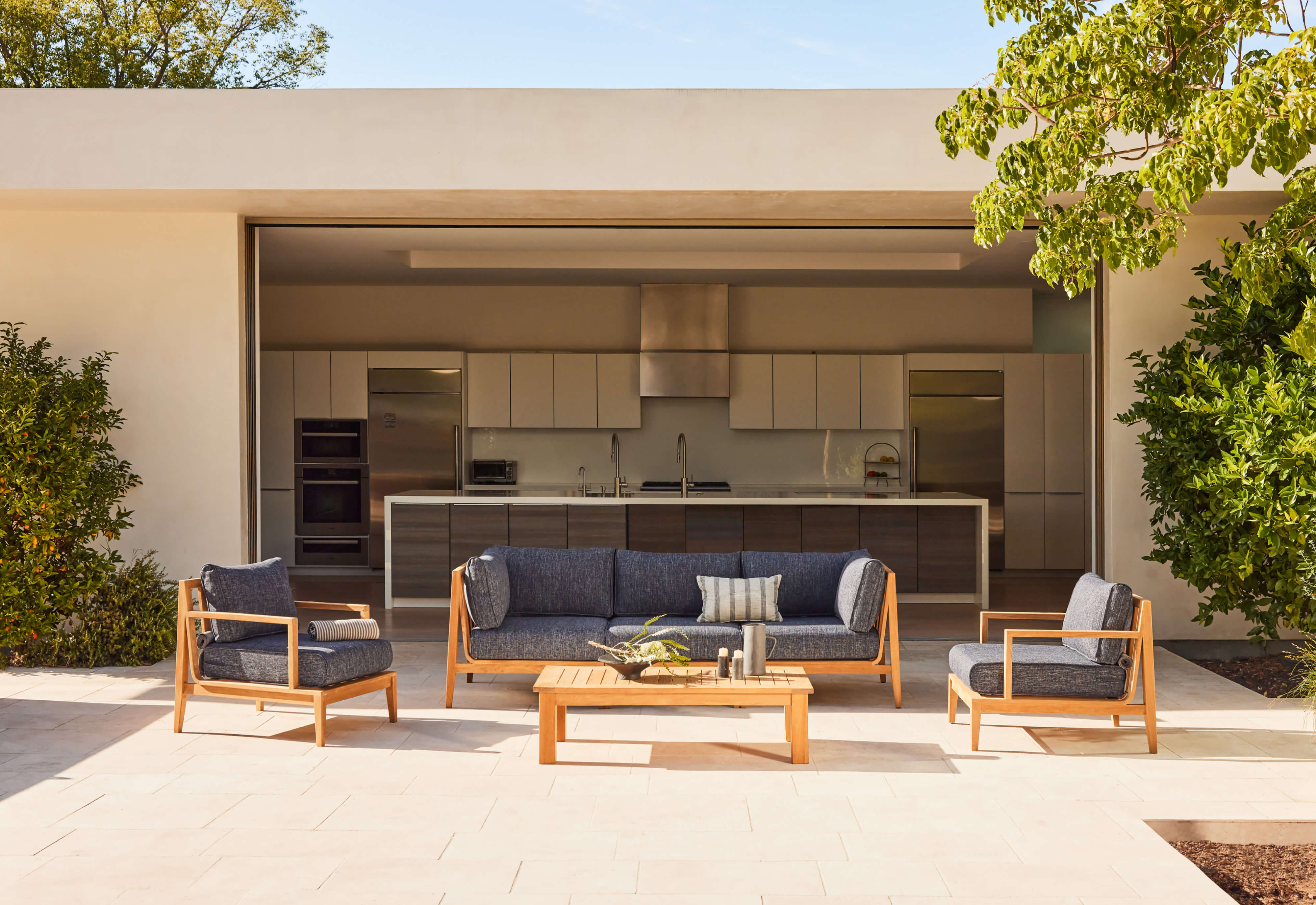 A teak outdoor sofa with matching armchairs arranged on a wooden deck, featuring navy blue cushions for comfortable seating.-teak outdoor sofa-outer