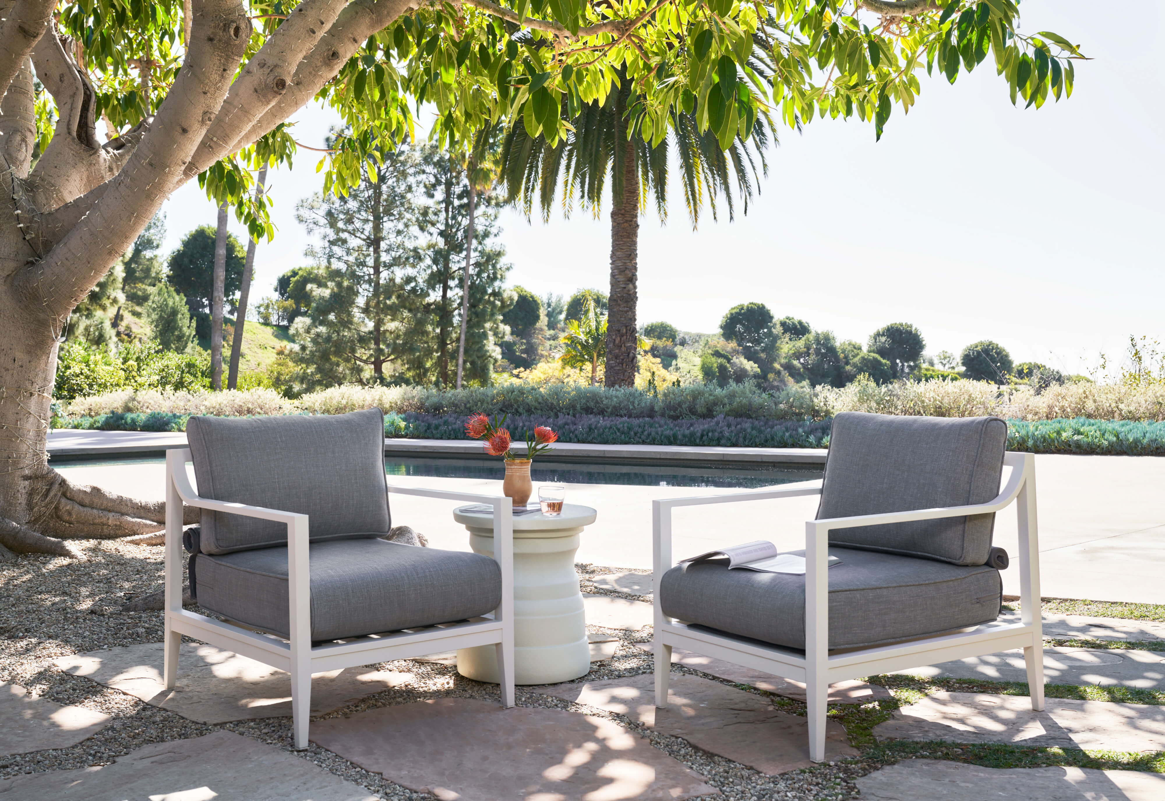 The white Tiered Concrete Outdoor Side Table coupled with two white aluminum outdoor armchairs and pebble gray fabric. #table color_(unavailable) white