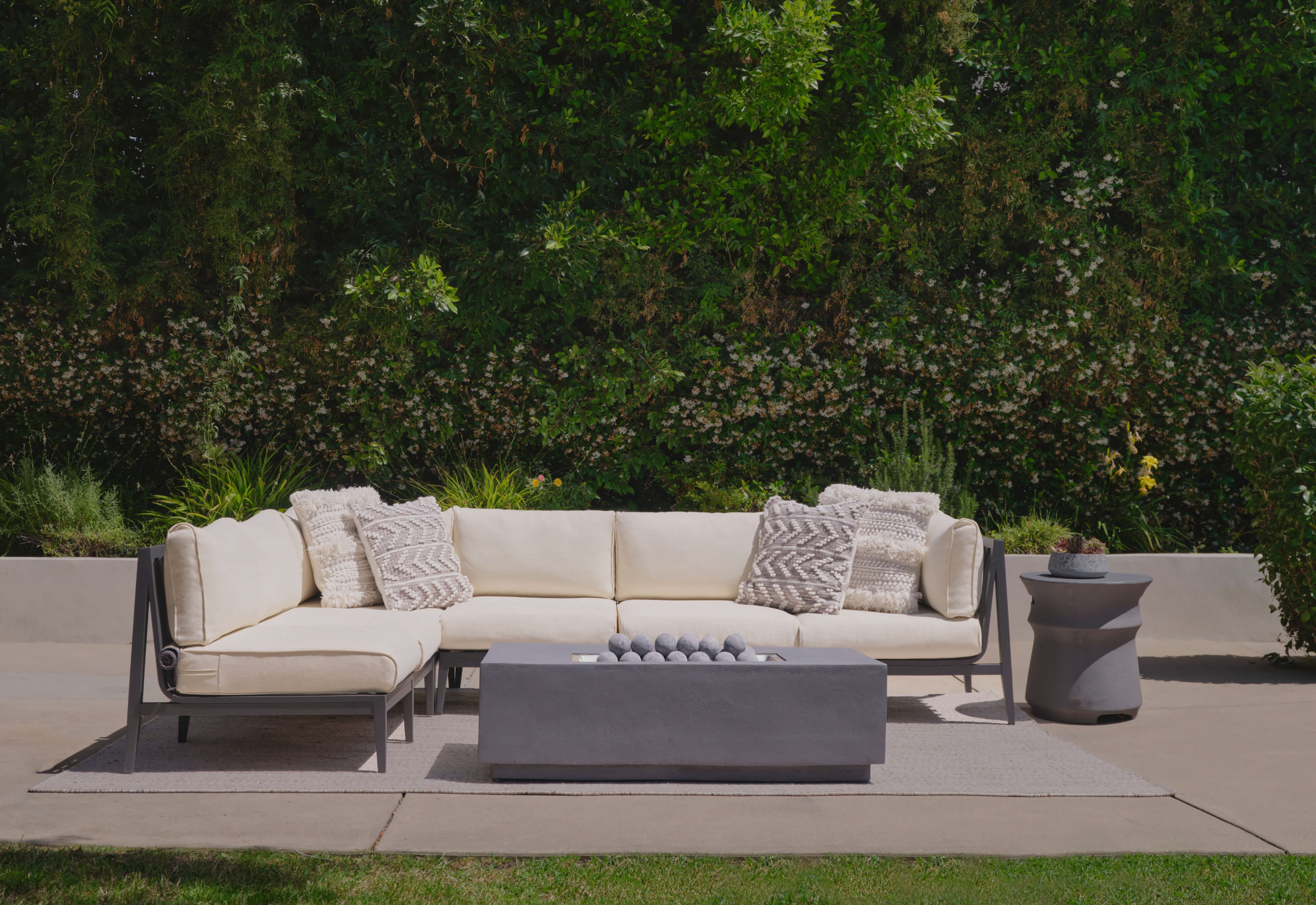 Charcoal aluminum L sectional with palisades cream cushions shown with the fire pit and classic concrete side table.https://liveouter.com/