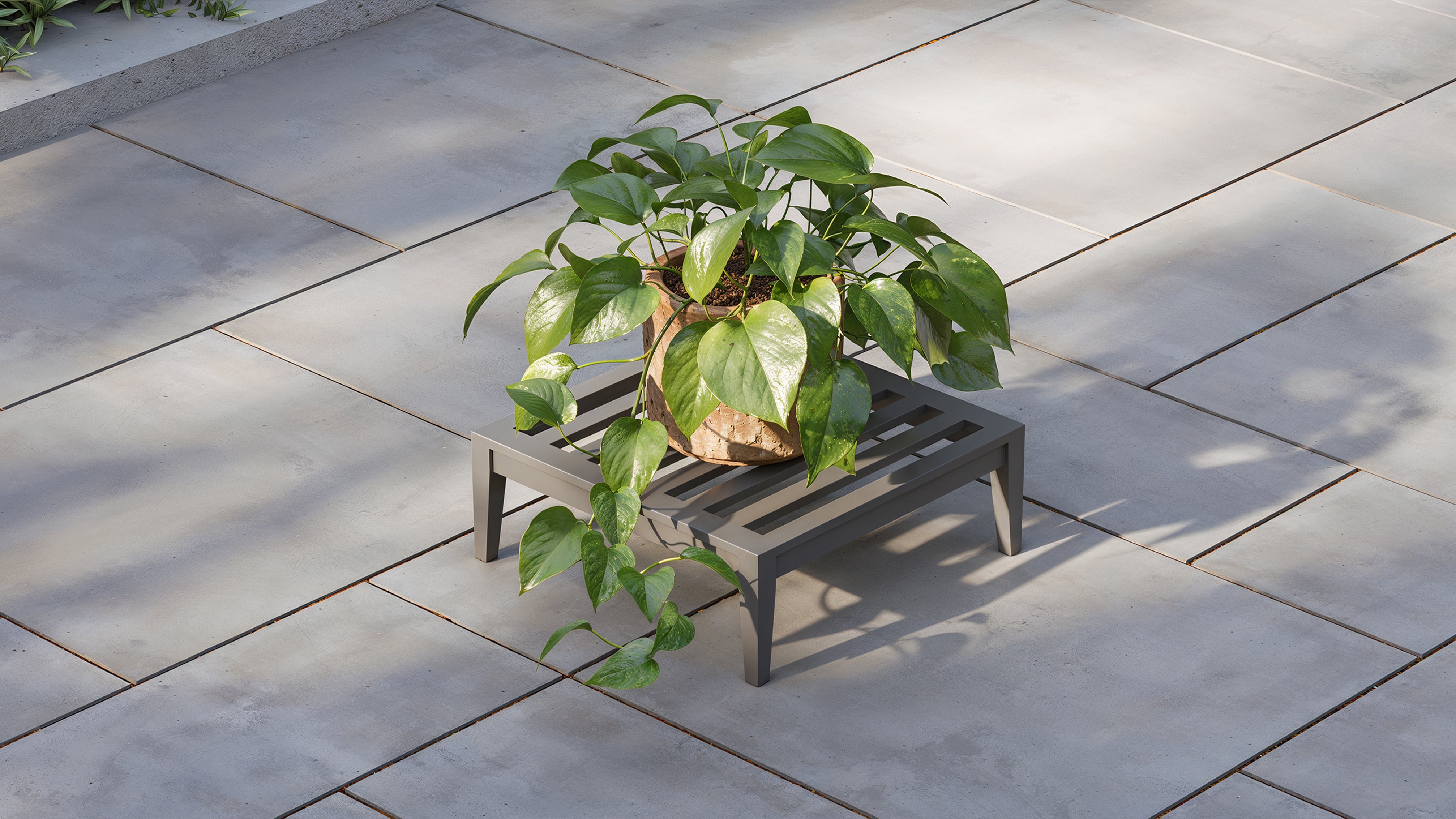 Outer charcoal outdoor ottoman used as patio side table with potted plant on modern stone terrace
