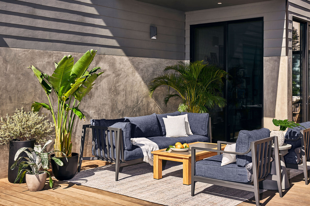 Charcoal aluminum outdoor sofa and armchairs with navy cushions beside a modern house.
