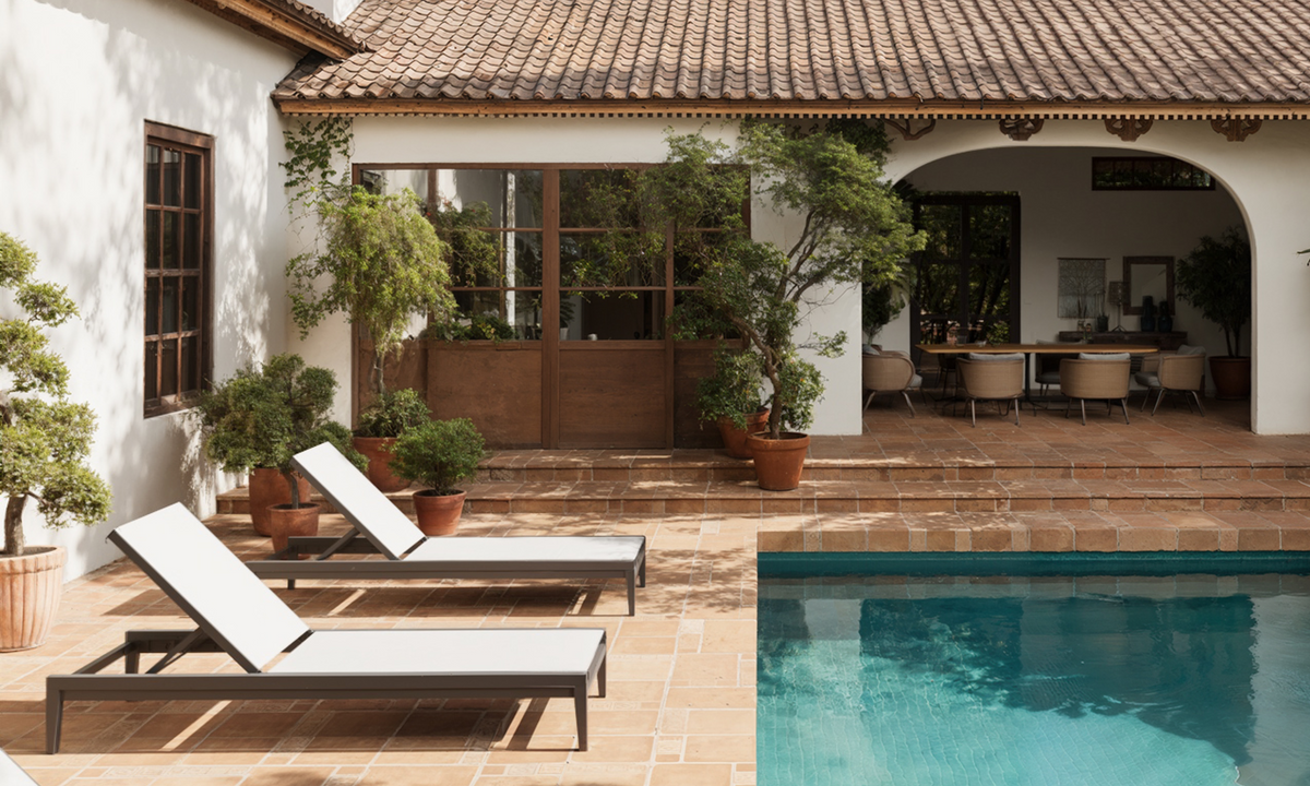 Two aluminum chaise lounges beside a courtyard pool, with a separate covered gathering space across the water.