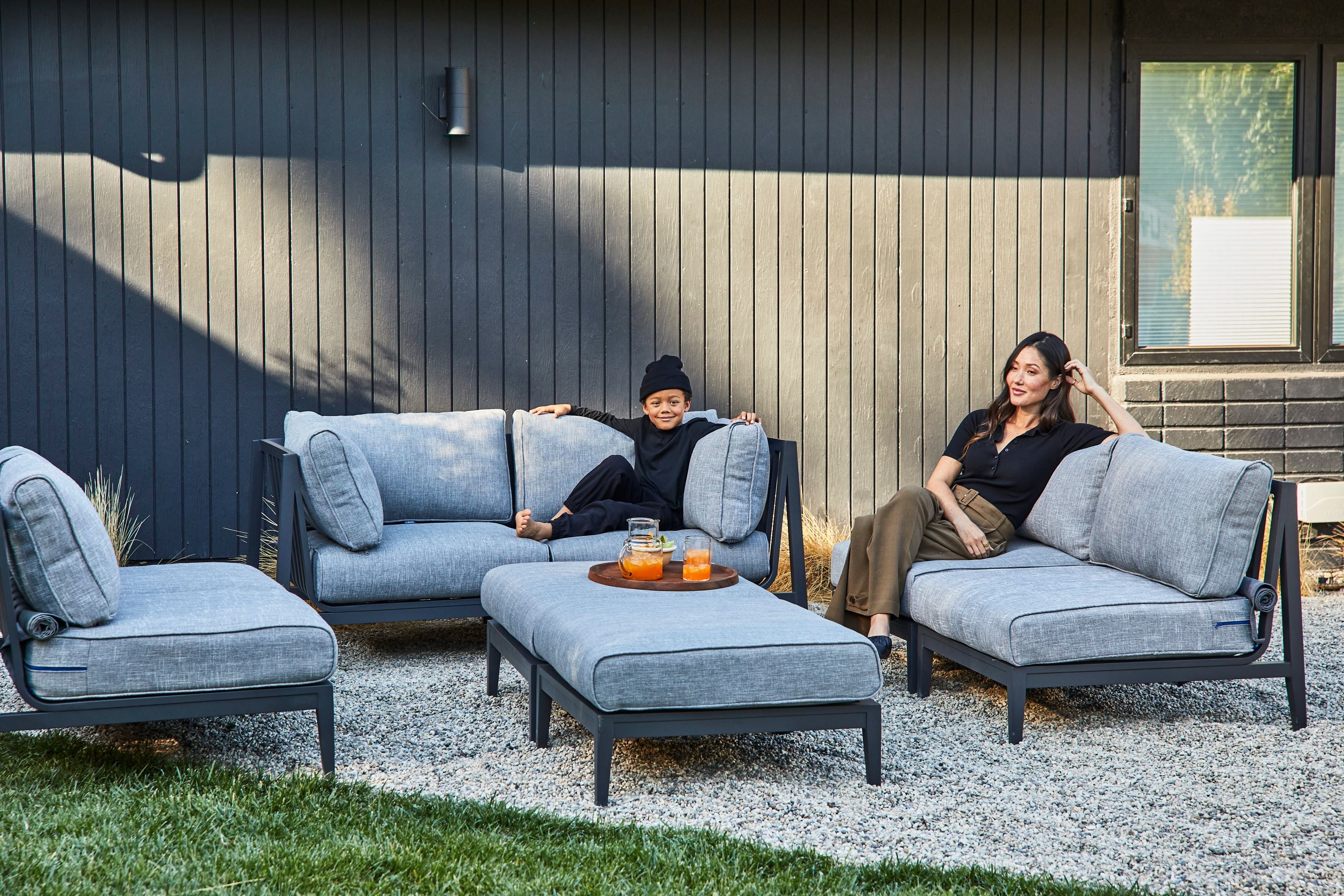 The charcoal aluminum sofa in pacific fog gray being enjoyed by a family, using the outdoor ottoman as a coffee table. 