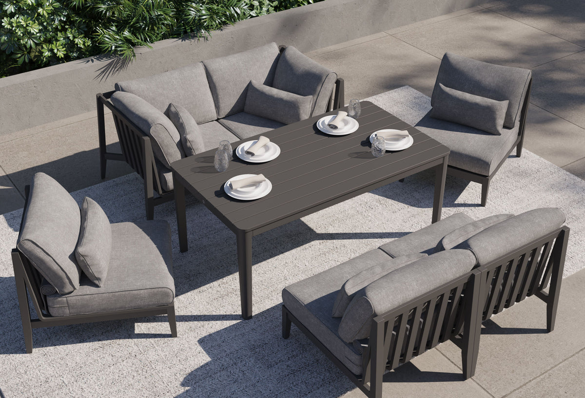 Cushioned charcoal aluminum outdoor seating grouped around a gathering-height table set with four plates and short drinking glasses.