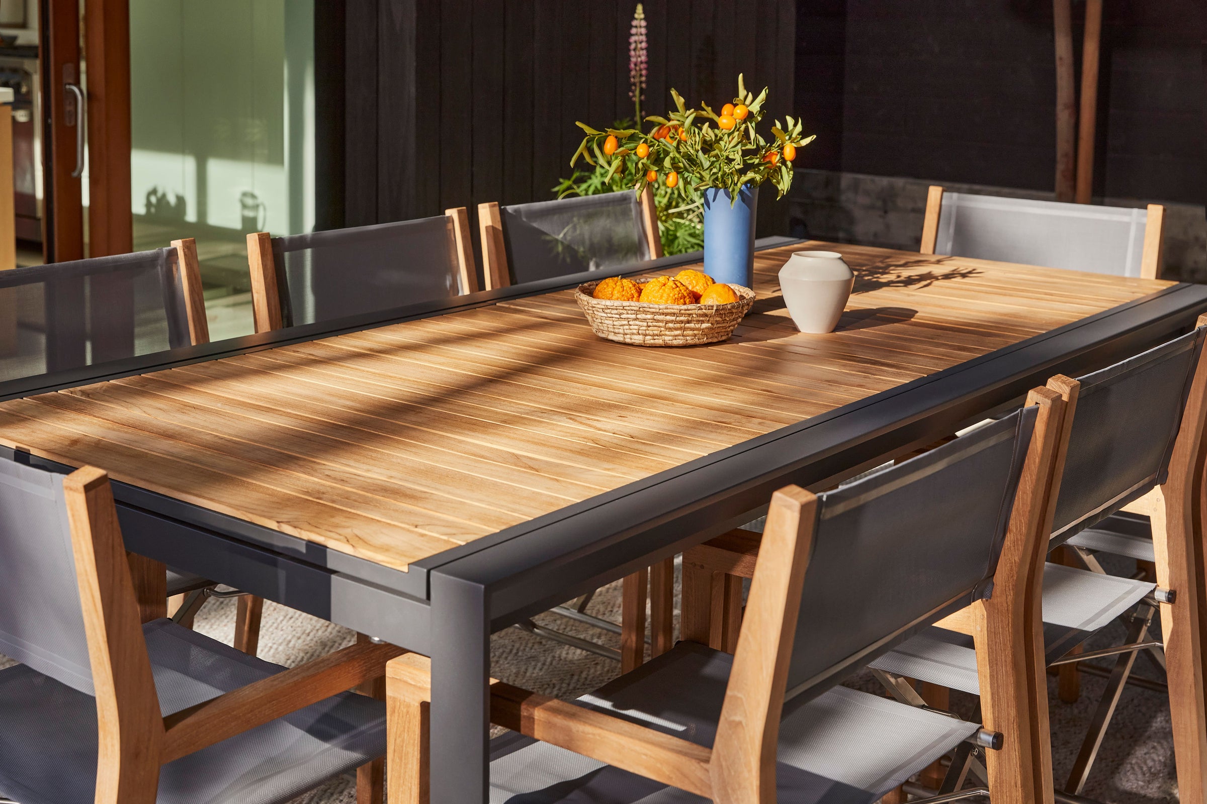 Close view of an Outer teak tabletop, powder-coated aluminum frame, and matching outdoor dining chairs