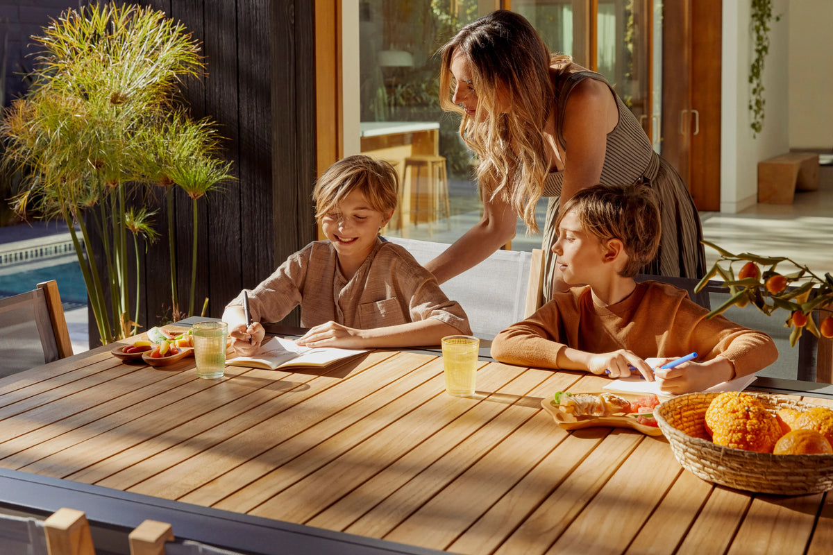 A parent and two children sharing a meal at an outdoor teak dining table