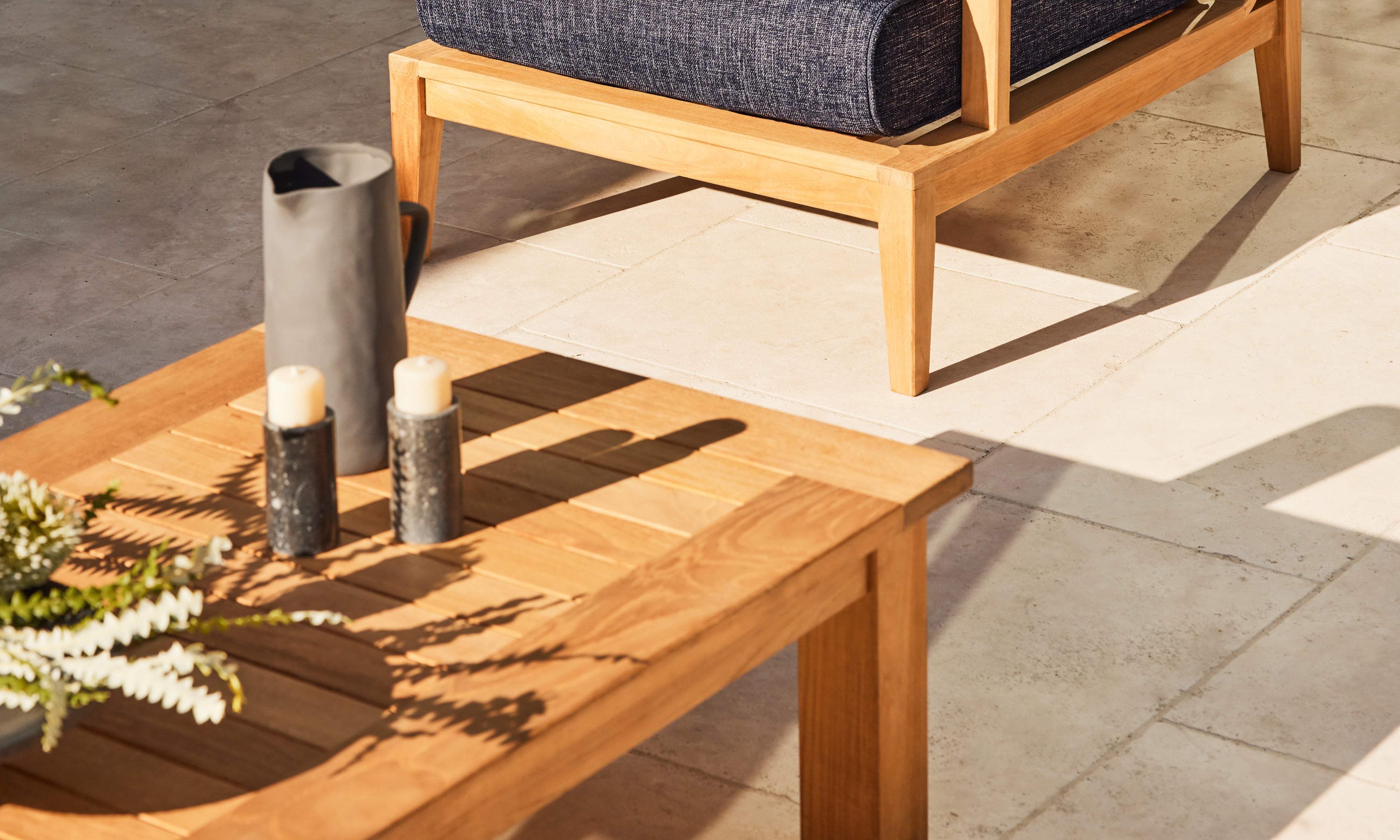 Outer teak outdoor coffee table with decorative accents beside lounge chair on sunlit modern patio