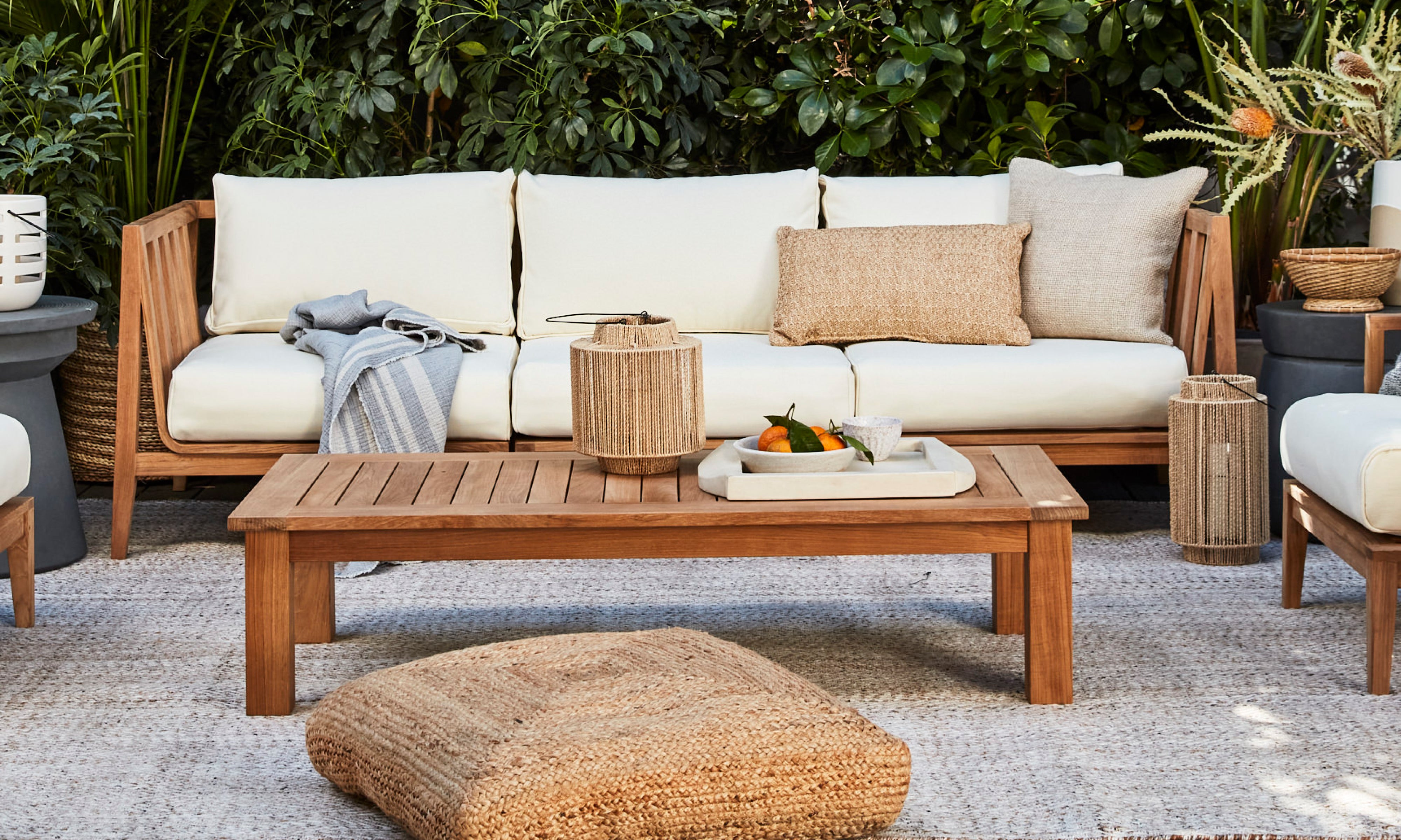 Outer teak outdoor coffee table styled with sofa seating in lush garden patio lounge setting