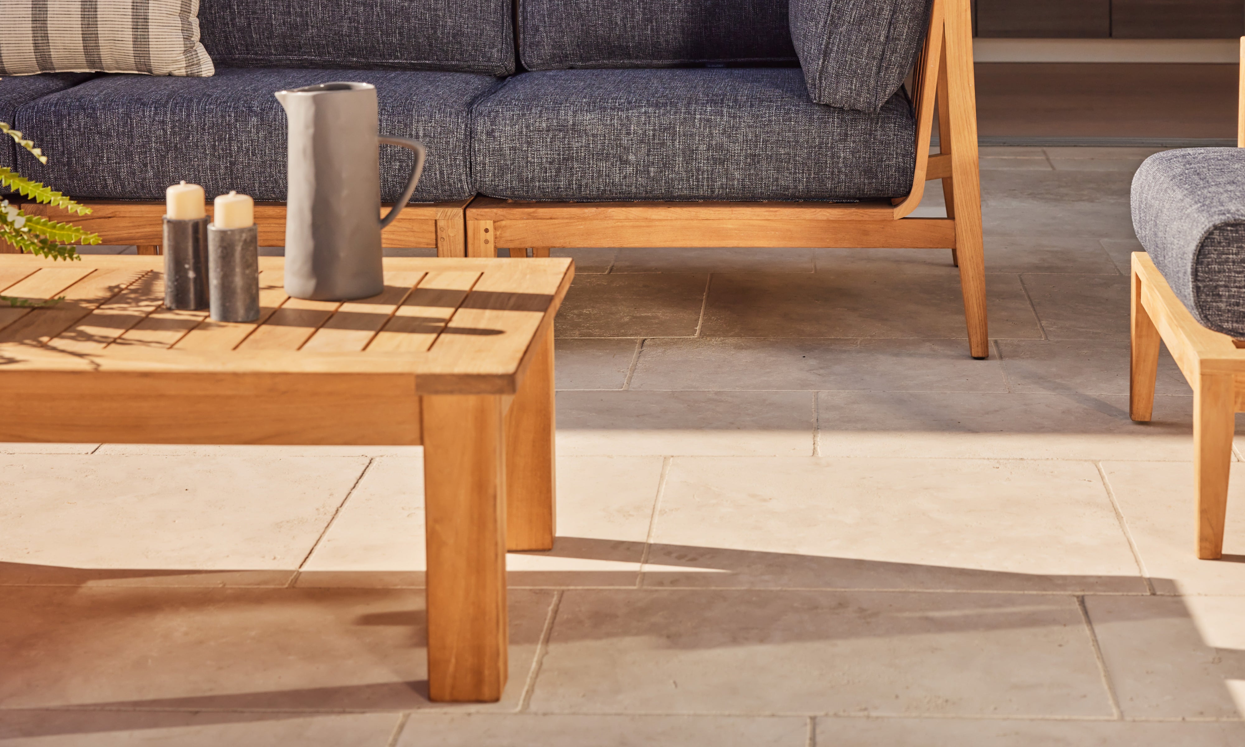 Outer teak outdoor coffee table with modern lounge seating and charcoal cushions on sunlit patio