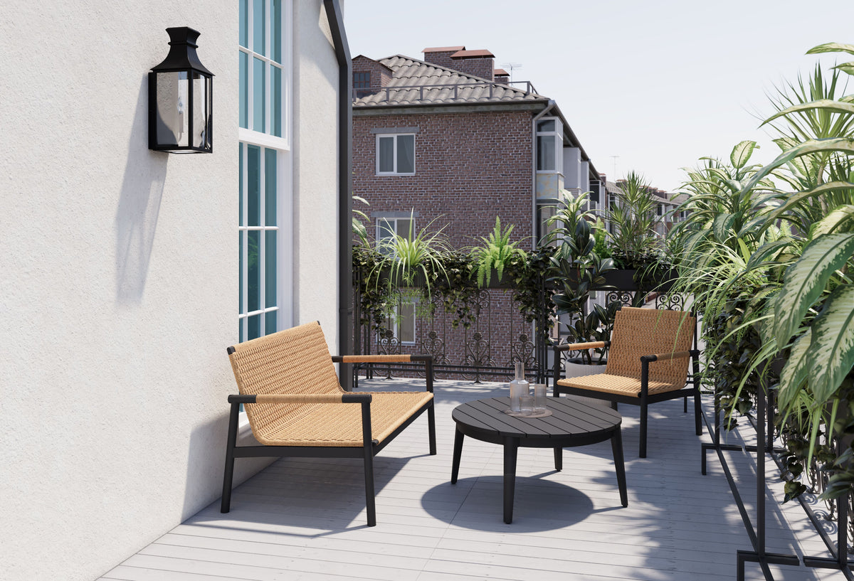 Two woven outdoor armchairs and a round table on a terrace beside a house.