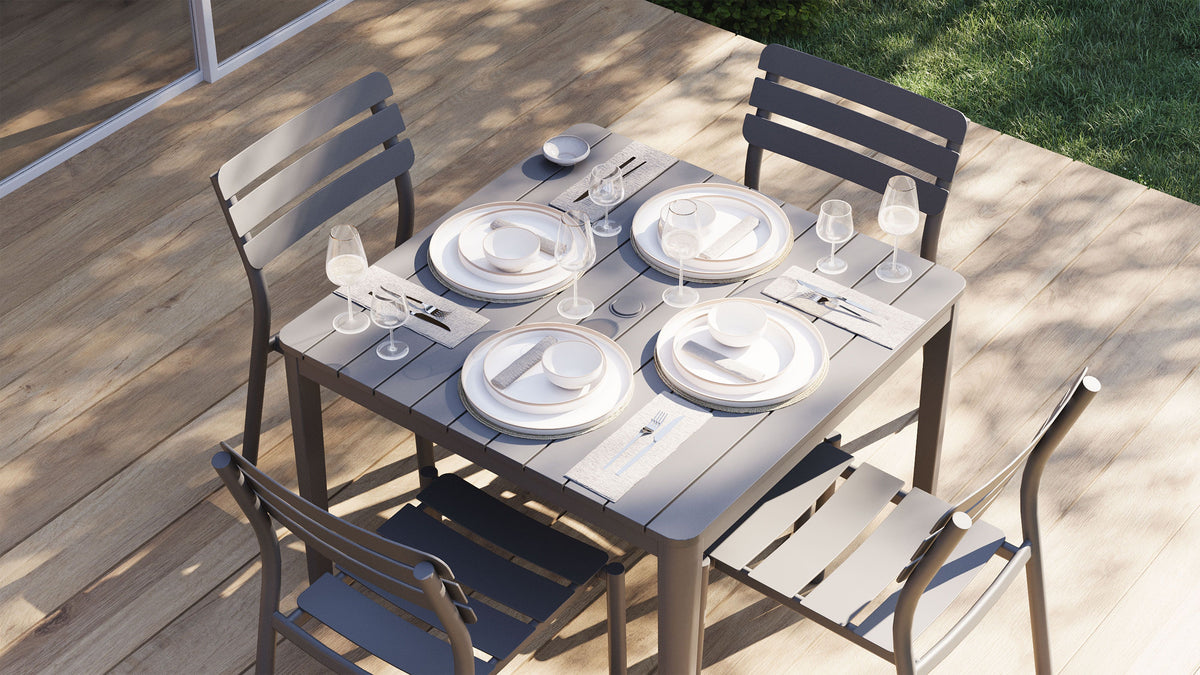 Overhead view of a square slatted aluminum dining table styled with four place settings, plates, bowls, napkins, and stemmed glasses.