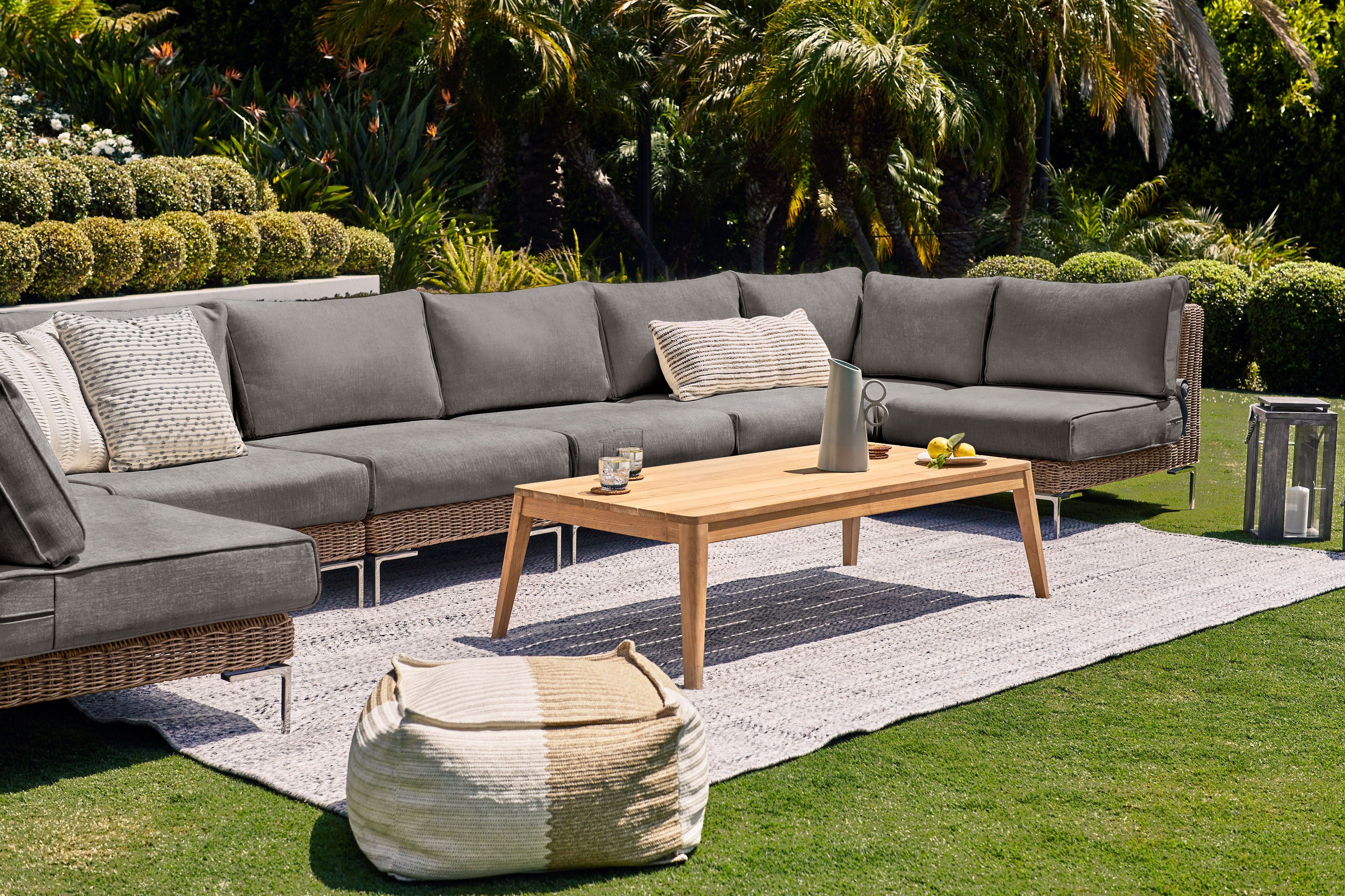 The 8 seat U sectional in brown wicker shown in a backyard with our tapered leg teak coffee table and seashell gray rug. #color_dark pebble gray