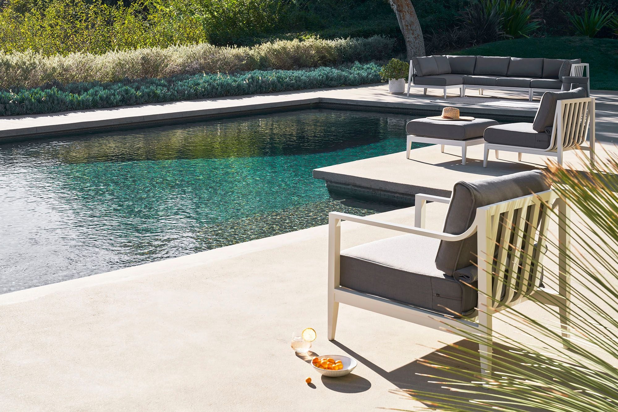 White aluminum armchairs in pebble gray shown poolside with the matching four seat sofa in the distance.
