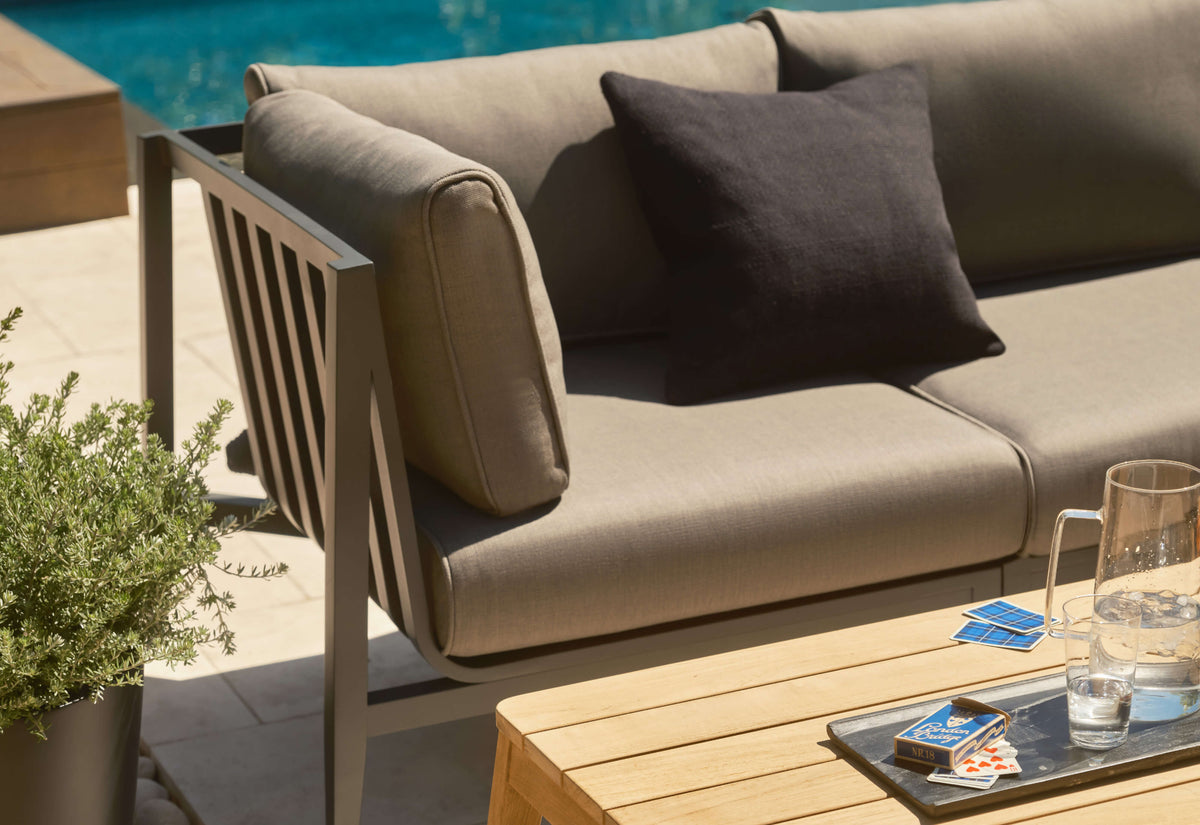 Close view of a charcoal aluminum sofa arm, seat cushion and back cushions beside a teak coffee table.