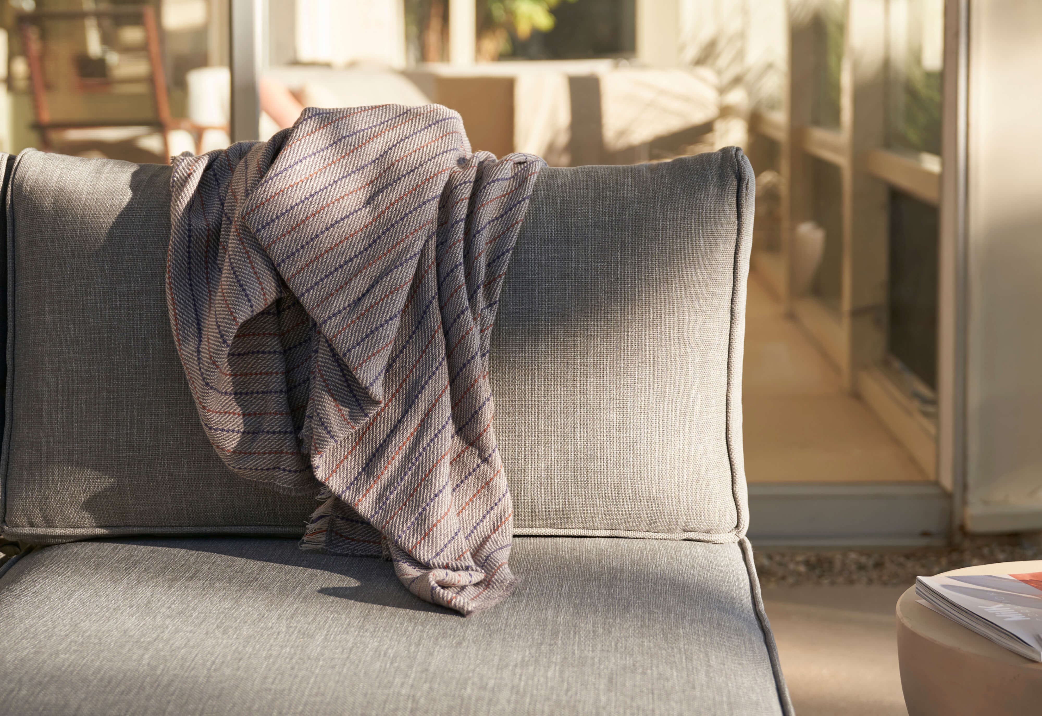 A closeup of the white aluminum armless loveseat with pacific fog gray fabric with a draped pinstripe bug shield blanket.