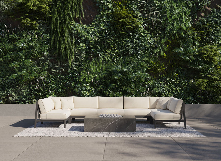 Beige U-shaped outdoor sectional surrounding a low-profile rectangular marble fire pit table against a vertical plant wall.