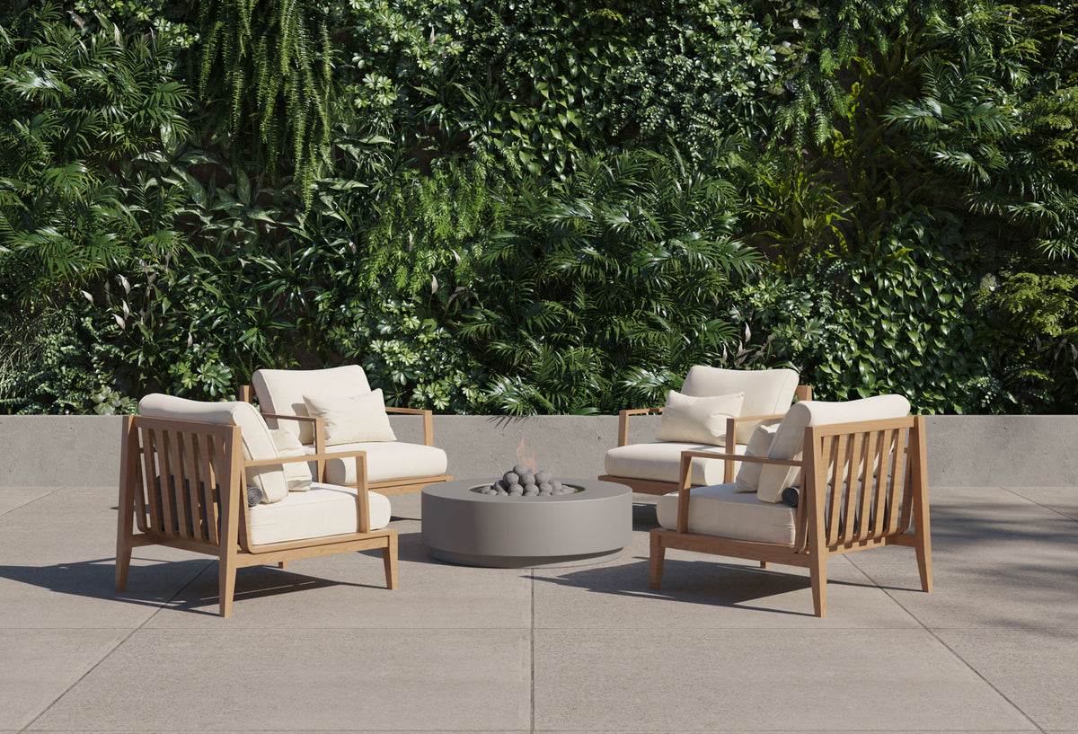 Four teak lounge chairs with cream cushions surrounding a round concrete fire pit table in a courtyard.