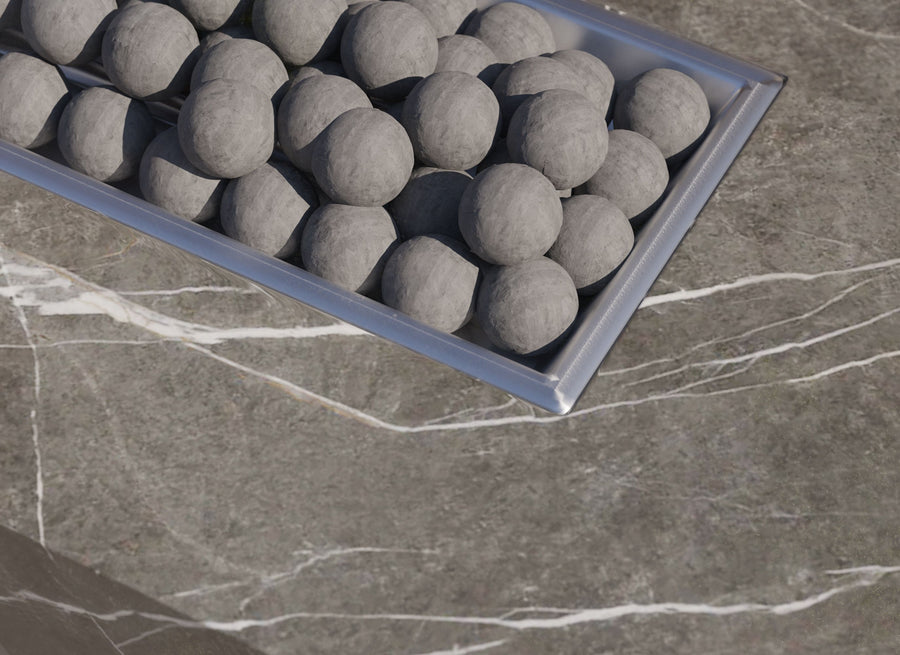 Top-down view of grey ceramic fire spheres inside a stainless steel burner pan on a marble fire pit table.