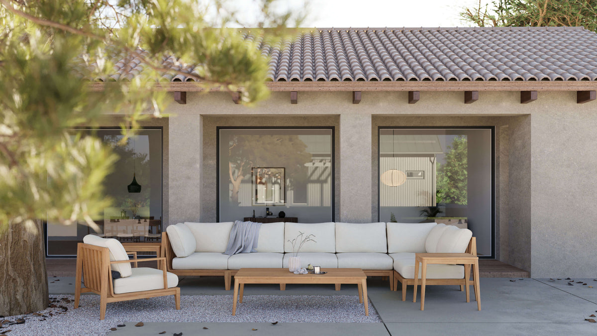 Cream-cushioned teak outdoor seating and wood tables arranged in front of broad black-framed glazing.